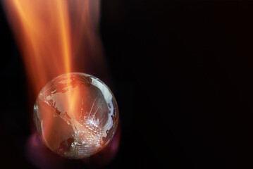 Glass planet earth on fire on black background, copy space.