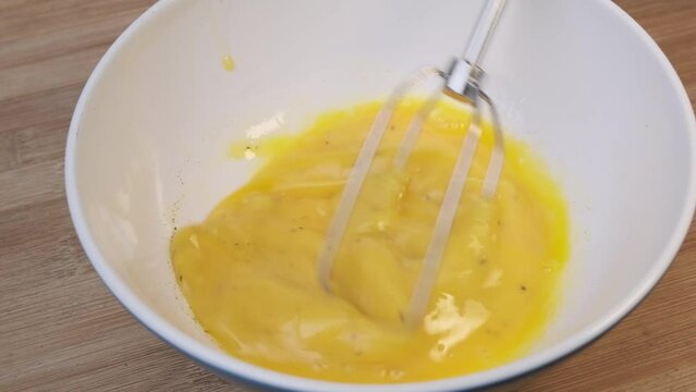 Hand whisking eggs in a bowl with a wire whisk preparing homemade omelette in the morning. Cooking breakfast. Healthy food concept.