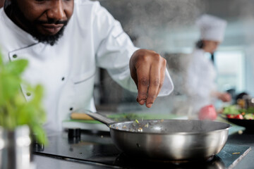 Master chef wearing cooking uniform garnishing gourmet dish with fresh chopped herbs in restaurant...