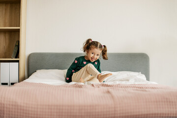 A charming little girl jumps on the bed and laughs