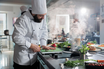 Head chef using professional cooking knife to smash a big head of fresh organic garlic to be added to gourmet dish. Food industry worker preparing recipe ingredients while in restaurant kitchen.