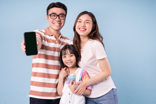 Image Of Young Asian Family Using Smartphone On Blue Background