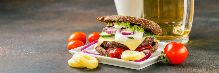 Hamburger on a plate and beer against a dark background. Unhealthy food. Snack. Selective focus.