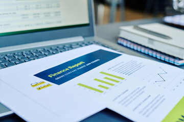 Financial papers with statistics and profit information on keyboard of laptop with analyzed data on screen at workplace of accountant