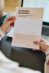 Hands of young male economist or analyst holding document containing financial budget breakdown data over laptop keyboard