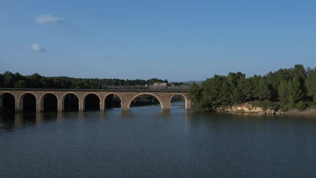 Aerial drone view flying over a reservoir and under a railway bridge in the afternoon light. El Reagajo. Castellon, Spain.