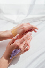 Obraz na płótnie Canvas Female hands applying purple cream scrub on skin top view white background. Skincare routine concept