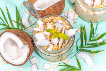 Breakfast overnight oatmeal oats with coconut milk and fresh coconut pieces. Diet healthy food, vegan diet. On light background with fresh coconuts and palm leaves, copy space