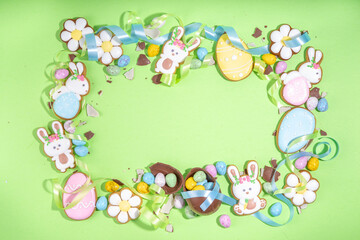 Happy Easter colorful flatlay. Colorful sugared and chocolate Easter eggs, sugar glazed cookies with festive holiday ribbon on light green background top view copy space