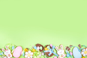 Fototapeta na wymiar Happy Easter colorful flatlay. Colorful sugared and chocolate Easter eggs, sugar glazed cookies with festive holiday ribbon on light green background top view copy space