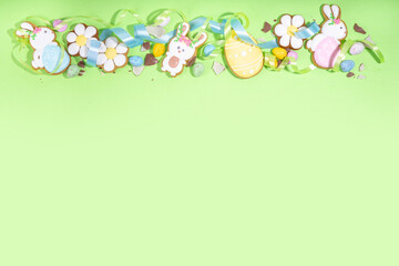Happy Easter colorful flatlay. Colorful sugared and chocolate Easter eggs, sugar glazed cookies with festive holiday ribbon on light green background top view copy space