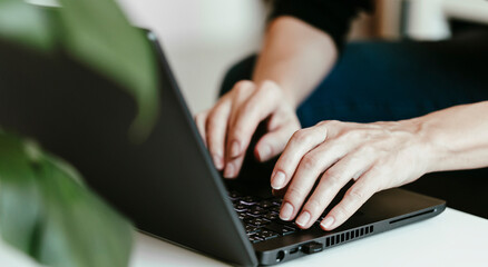 Young woman typing on laptop. Working at home, freelancer job concept, day light dynamic workplace.