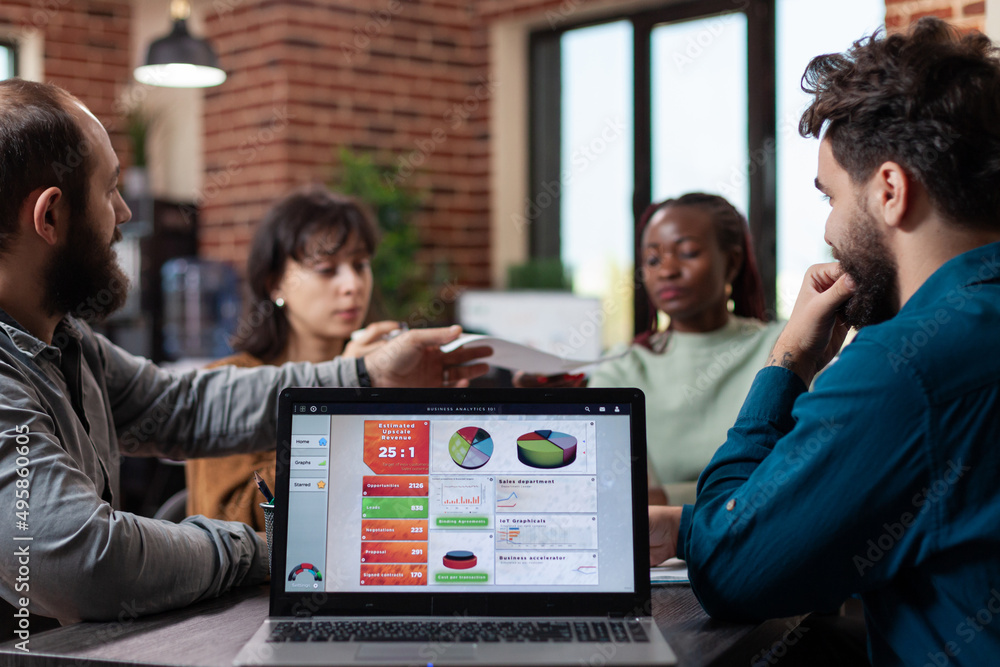 Poster laptop computer with marketing graphs on screen standing on table in startup office while diverse te