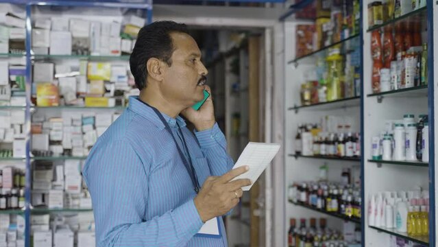 pharmacist talking on mobile phone with customer about prescription while checking stock at retail pharma store - concept of customer service, communication and small business.
