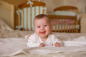 a kid in a white bodysuit is lying on the bed at home smiling