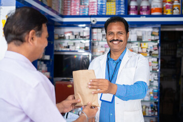 Smiling pharmacis giving medicine cover to customer at pharmacy shop - concept of customer service, professional occupation and happiness.