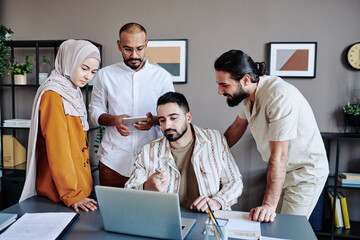 Young confident businessman pointing at data on laptop screen while making presentation for...
