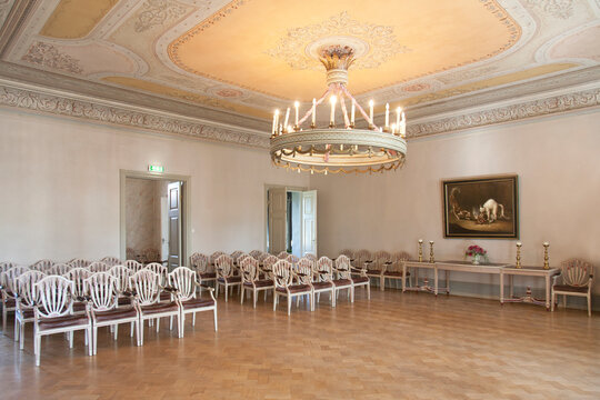 A large room with parquet flooring, elegant chairs and tables, chandelier and dance floor.