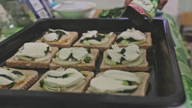 Adding herbs to toasts on a tray ready to be baked.  Home made slow food preparation with spicy jalapeno and mozzarella cheese. Green spicy toasts.