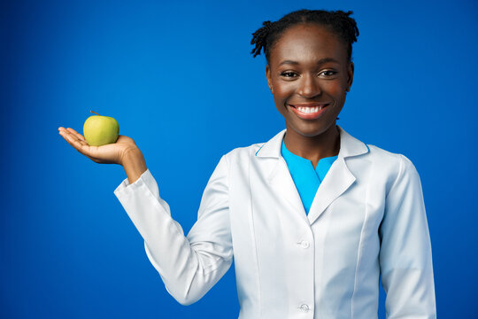 Beautiful african woman dietologist holding apple in her hand in blue studio