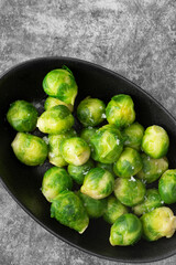 Brussels sprouts seasoned with sea salt in a black dish. On a stone background