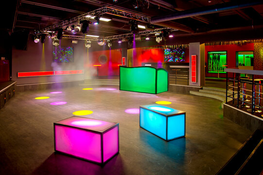 Nightclub interior, colourful lighting, wall screens and light boxes on a dance floor. 