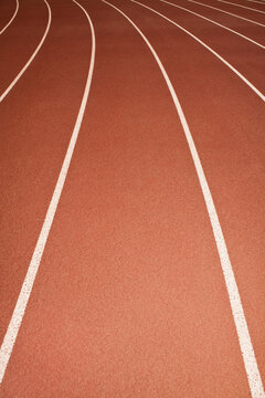 The surface of a sports athletics running track, red surface with white painted lane markings. 