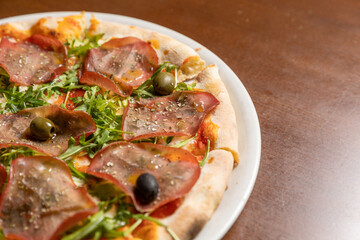 Arugula prosciutto pizza served on white plate