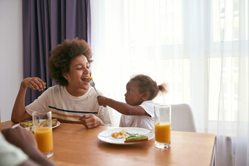 Obraz na płótnie Canvas Girl feeding her brother egg from fork near father