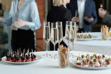 Two plates with appetizing canape and group of champagne in flutes standing on served tables prepared for celebration - obrazy, fototapety, plakaty
