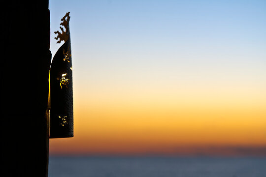 A lantern grille on a wall, silhouette against the sunset sky.