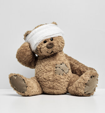 Children's toy teddy bear sits with a bandaged head. Childhood trauma concept