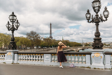 Pretty faceless girl in hat admiring the view from pont Alexandre III to Eiffel Tower. Old forged...
