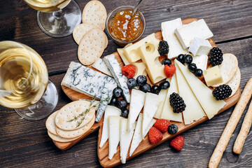 Сheese gorgonzola parmesan brie or camembert and maasdam. served with berries and crackers. cheese on a wooden board.