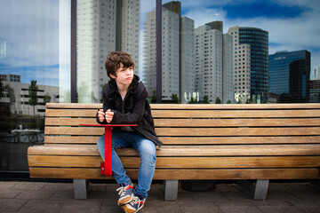 Pensive young teenage boy sitting on a bench in the street, looking aside. Netherlands, Rotterdam.