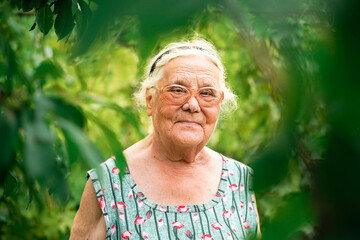 close up portrait of a senior woman in a garden. Very old lady of eighty years old wearing glasses.