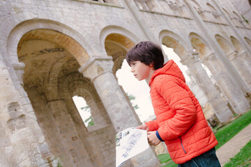 Obraz na płótnie Canvas Child visiting ruins of monastery Abbaye de Jumièges in Normandy, France. Boy holding museum plan in his hands.