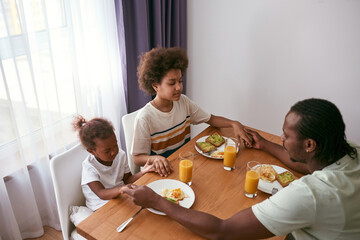 Father, daughter and son praying before breakfast