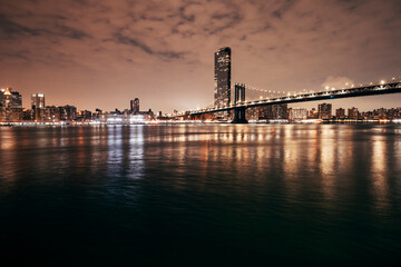 manhattan bridge and new york city skyline at night by the bay