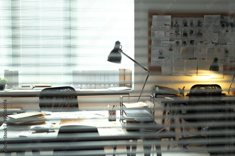Poster part of small office of fbi agents with lamp lighting desk against board with criminal profiles cont