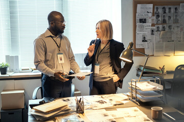 Young serious African American male FBI agent listening to mature female colleague in formalwear...