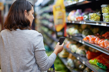 The smart way to shop. Cropped shot of a woman checking her digital shopping list on her cellphone in a grocery store.