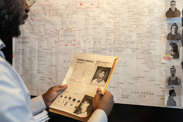 Young African American male FBI agent looking through criminal profile of gang leader in front of...