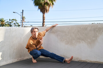 Man dancing touching wall outdoors with blue sky power lines and palm tree 