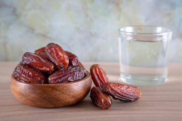 Glass of water with a bowl of date fruit on a wooden background.Muslims break the fast with water and dates