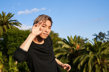 Man posing with hand by face outdoors with blue sky and palm tree