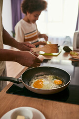 Dad fry eggs on pan and son smear kiwi on bread