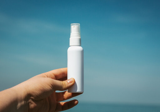  Girl's hand holding cosmetic spray bottle outside in front of sea coast. Idea for fresh marine scented cosmetics mock up.