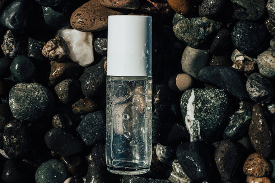 Close up of a beauty product transparent bottle on wet beach stones . Fresh ocean scented product mock up. 