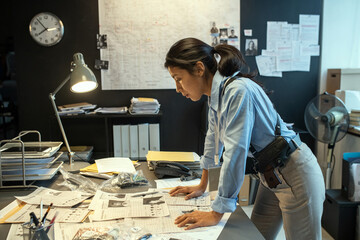 Side view of young serious female detective learning personal information of criminal authority or...
